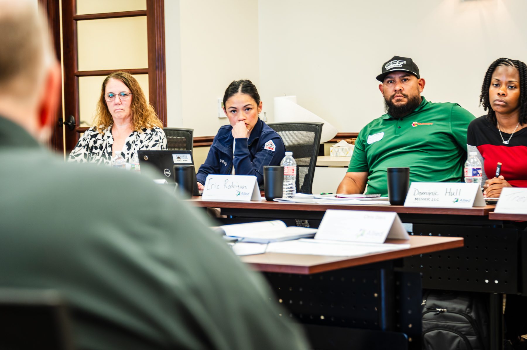 Diverse group of professionals engaged in a meeting or training session, focusing on collaboration and discussion, with name tags visible on the table.
