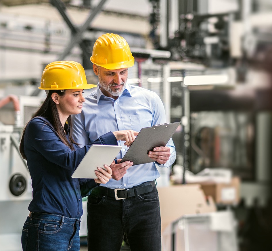 Two construction professionals in hard hats review project documents in an industrial setting, emphasizing teamwork and safety in the workplace.
