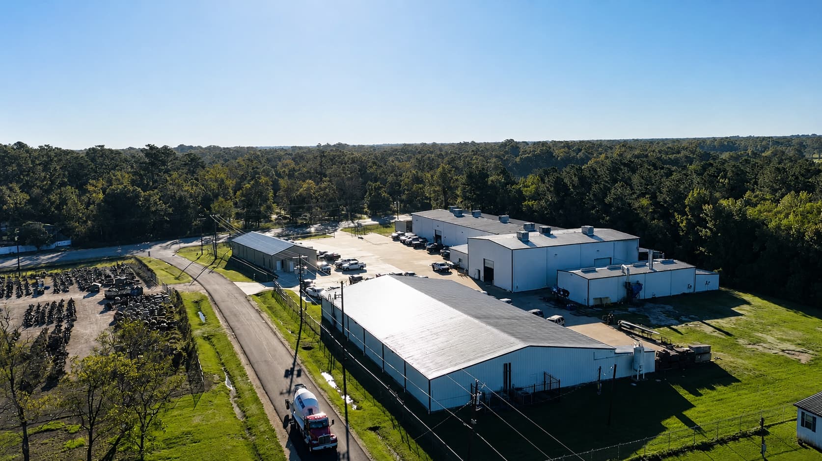 Aerial view of a Texas rotating equipment facility featuring multiple industrial buildings, vehicles parked in the lot, and surrounding greenery under a clear blue sky.
