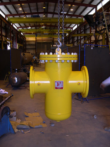Yellow bolted-cover strainer hanging from a chain in an industrial workshop, showcasing its multi-port design and robust construction, ideal for fluid filtration applications.