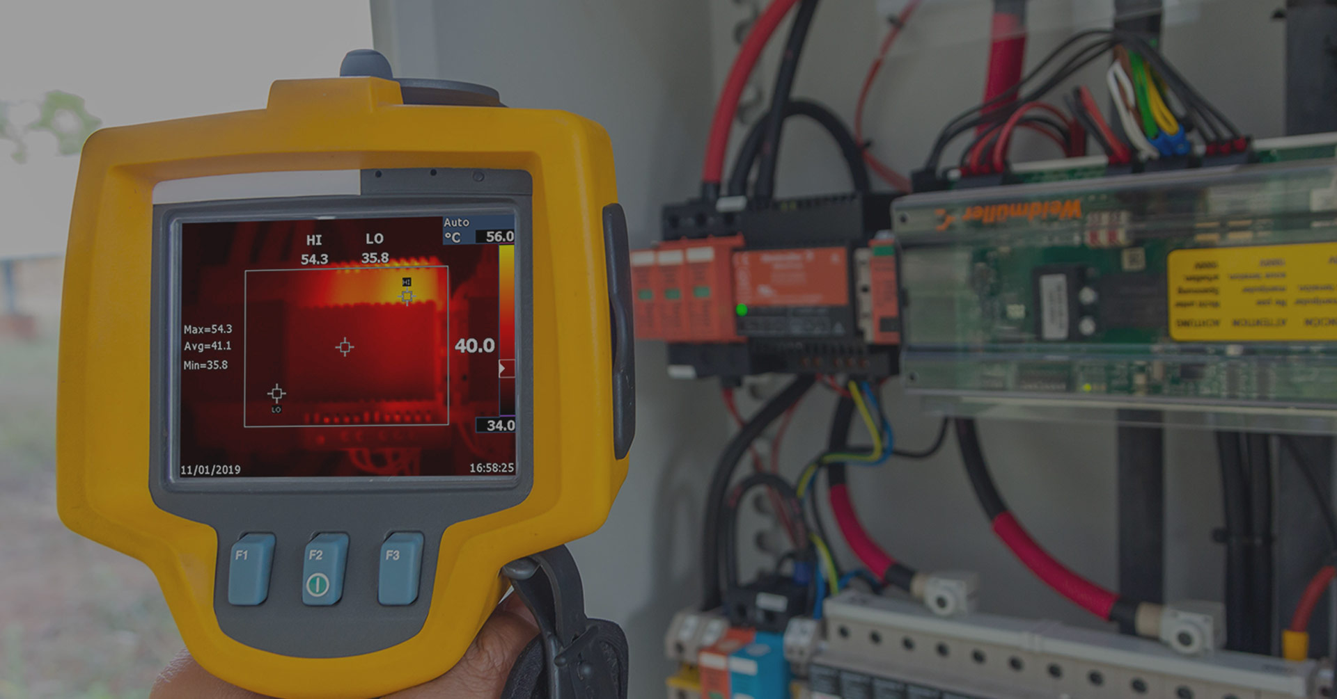 Thermal imaging camera displaying temperature readings while monitoring electrical components inside a control panel, highlighting potential hotspots for maintenance and safety inspections.