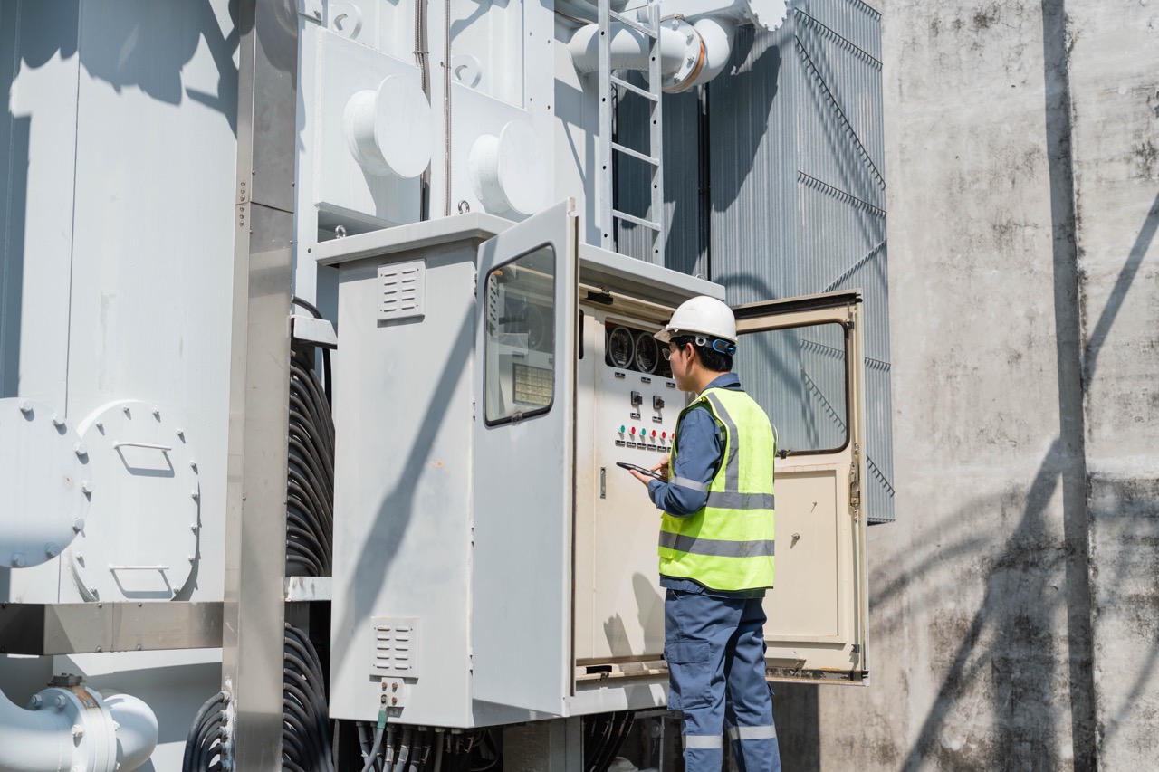Technician in safety gear inspecting control panel of electrical equipment outdoors, emphasizing safety and maintenance in power management.