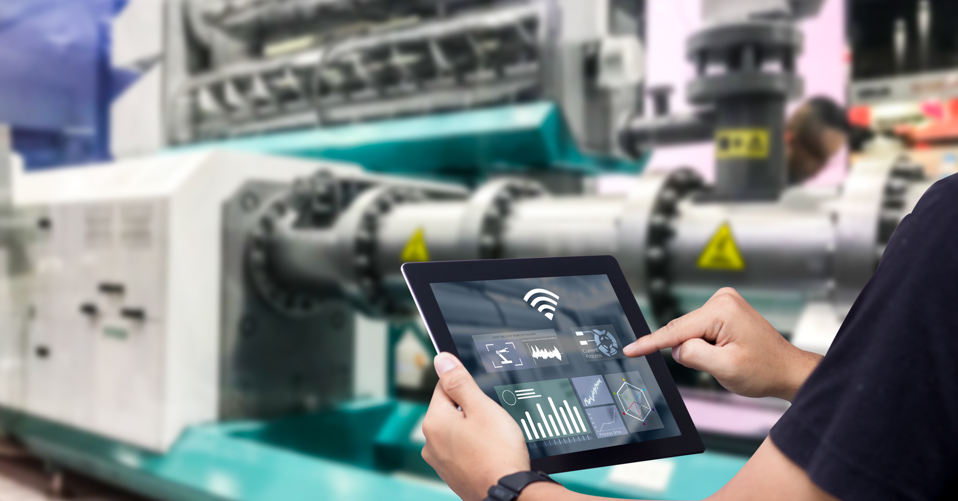 Person using a tablet to monitor and control industrial machinery, showcasing digital interfaces and data analytics in a manufacturing environment.