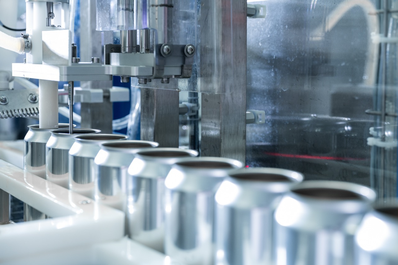 Automated can filling machine in a beverage production facility, showcasing a close-up view of aluminum cans on the assembly line, highlighting the precision and efficiency of modern packaging technology.