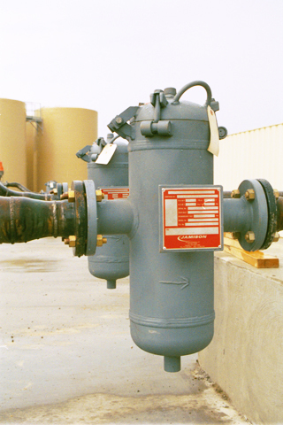 Loading rack basket strainers installed on a pipeline, featuring a cylindrical filter housing with a label and directional arrow, designed for efficient filtration in industrial applications.