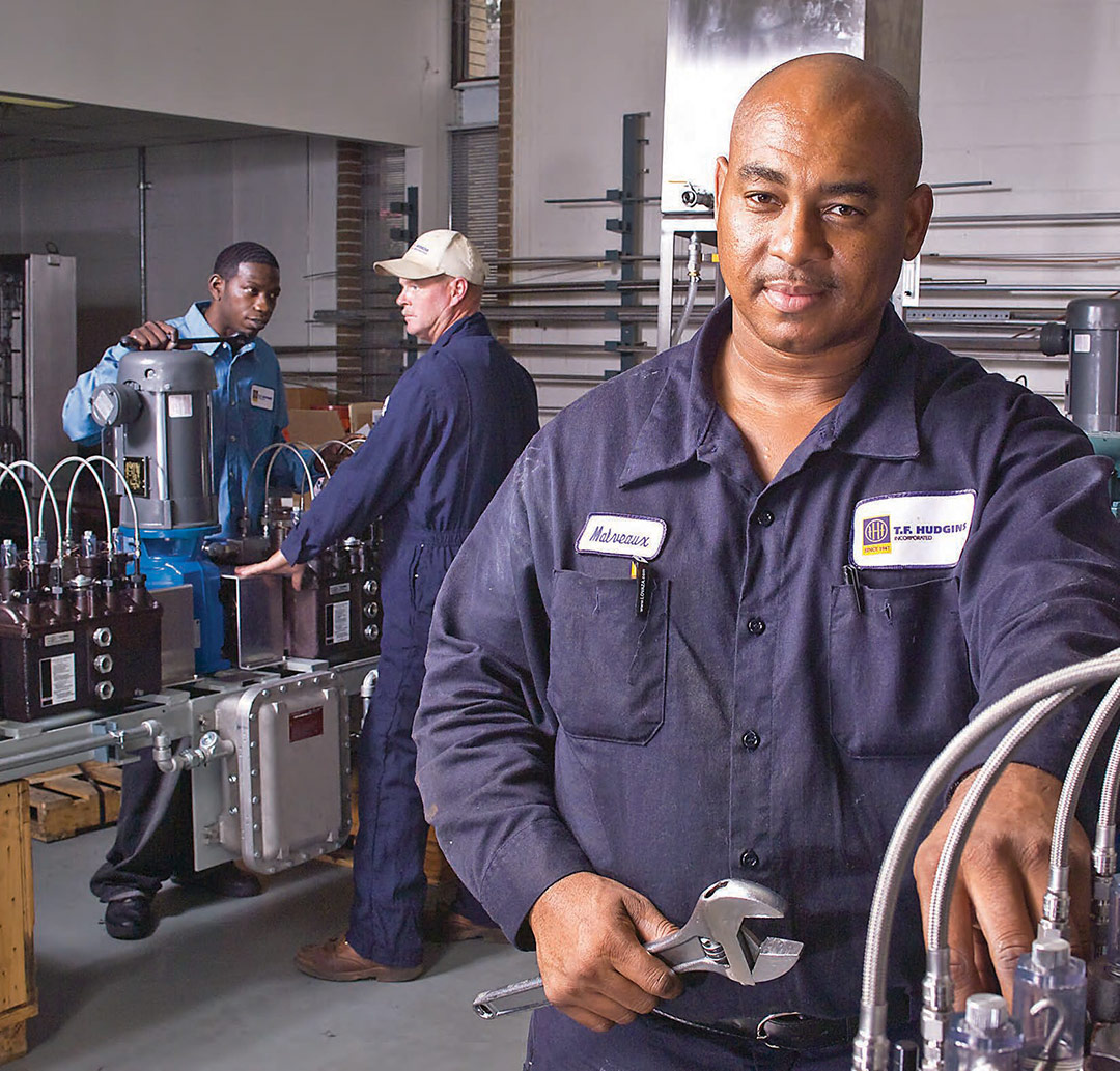 Technicians working on lubrication systems in a workshop, with one holding a wrench and others assembling components.