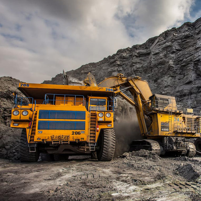 Heavy mining equipment, including a large yellow dump truck and an excavator, operating in a rugged quarry environment, showcasing the industrial use of Stratus diesel particulate filters.