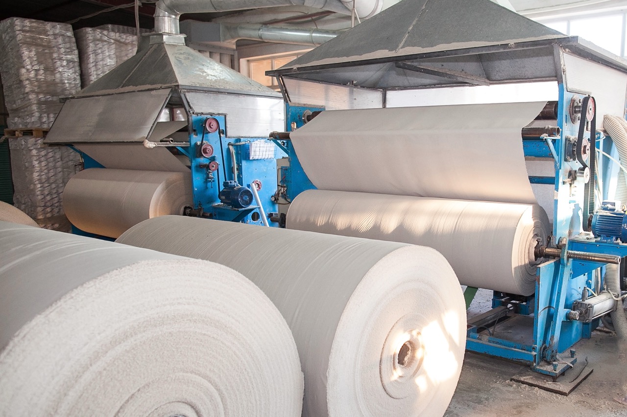 Industrial paper manufacturing machine with large rolls of unprocessed paper in a factory setting, showcasing the production process of paper rolls.