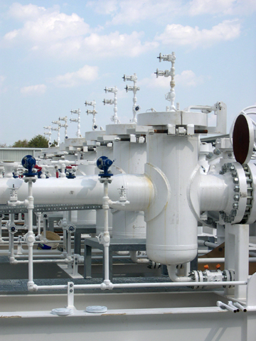 Oil basket strainers installed on industrial piping system, featuring multiple strainers, valves, and gauges against a clear sky backdrop.