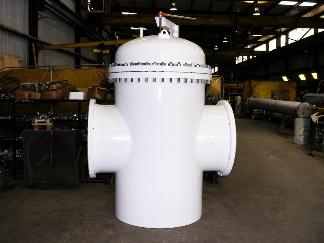 Large white pump protection basket strainer positioned in an industrial workshop, showcasing its robust design and dual side outlets for effective filtration in fluid systems.