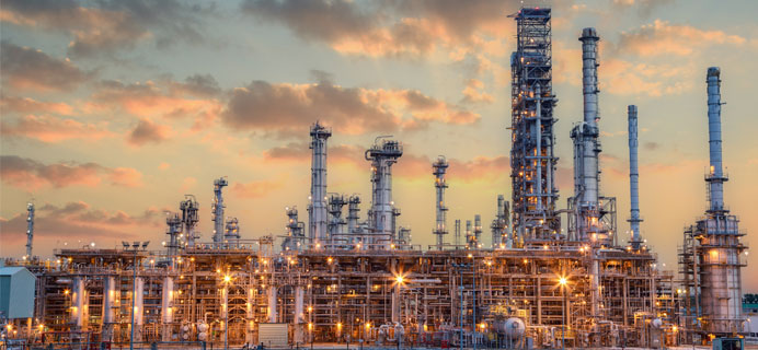Industrial facility with multiple towers and pipelines at sunset, illustrating the complexity of lubrication system repair in manufacturing environments.