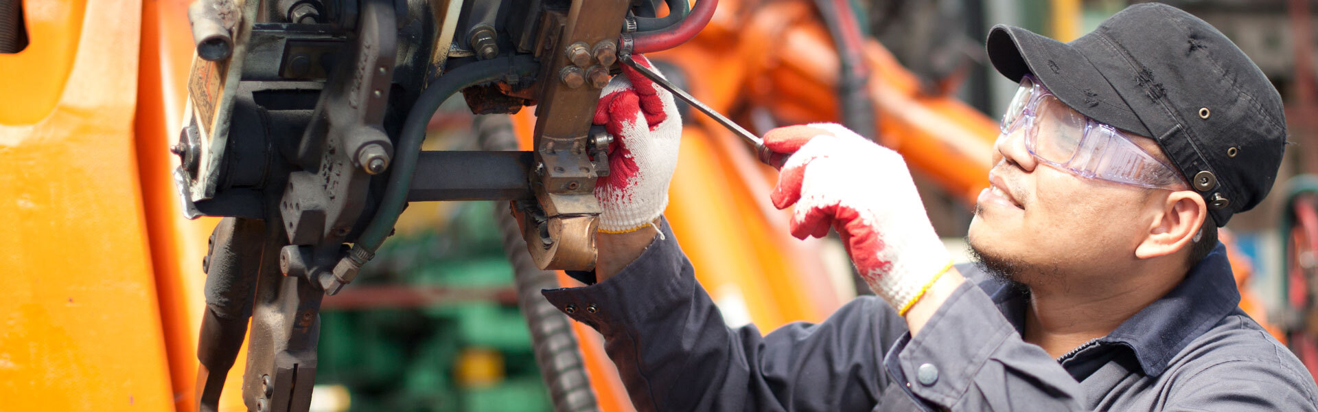 A mechanic wearing safety glasses and gloves inspects and repairs machinery in an industrial setting, highlighting hands-on maintenance and safety practices in equipment management.