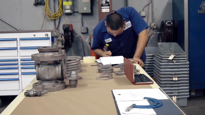 Technician conducting lubrication system repair, reviewing components and taking notes at a workbench with various parts and tools organized around him.