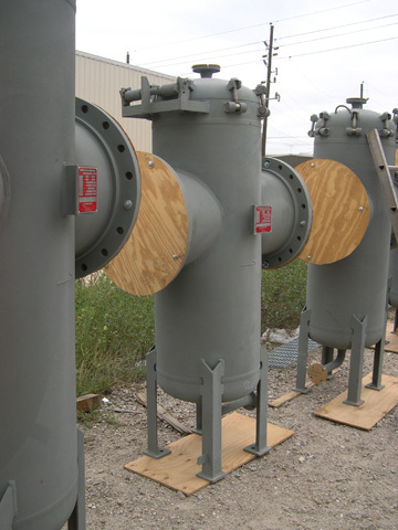 Industrial water basket strainers lined up outdoors, showcasing their cylindrical design and wooden end covers, essential for filtering debris from water systems.